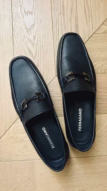 Schwarze Ferragamo-Loafer mit Metallspange auf Holzboden